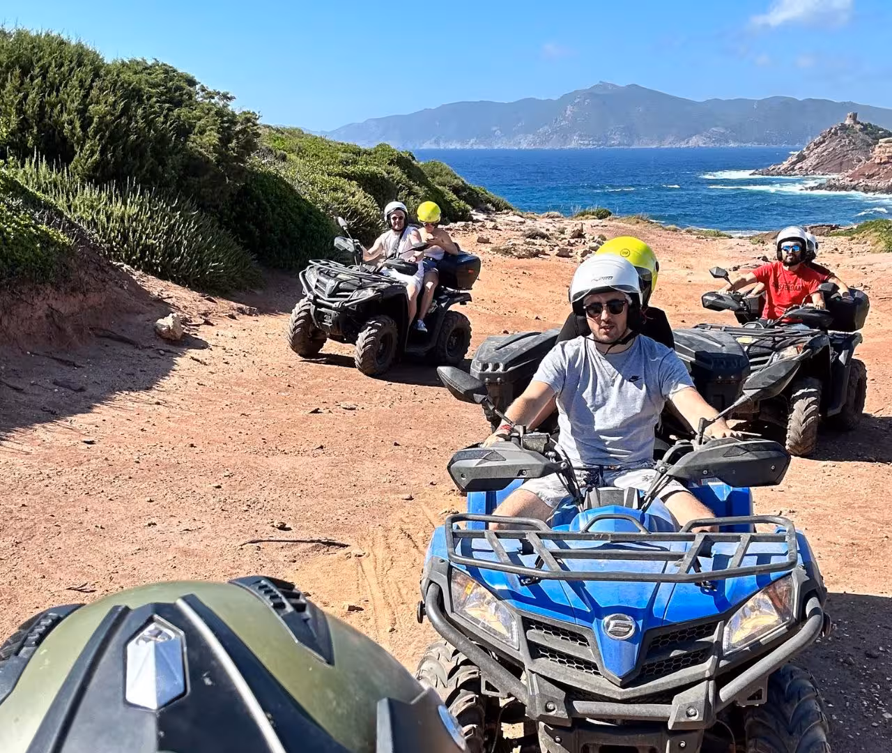 Group enjoying Alghero quad tour along scenic coastline with rugged terrain and ocean views.