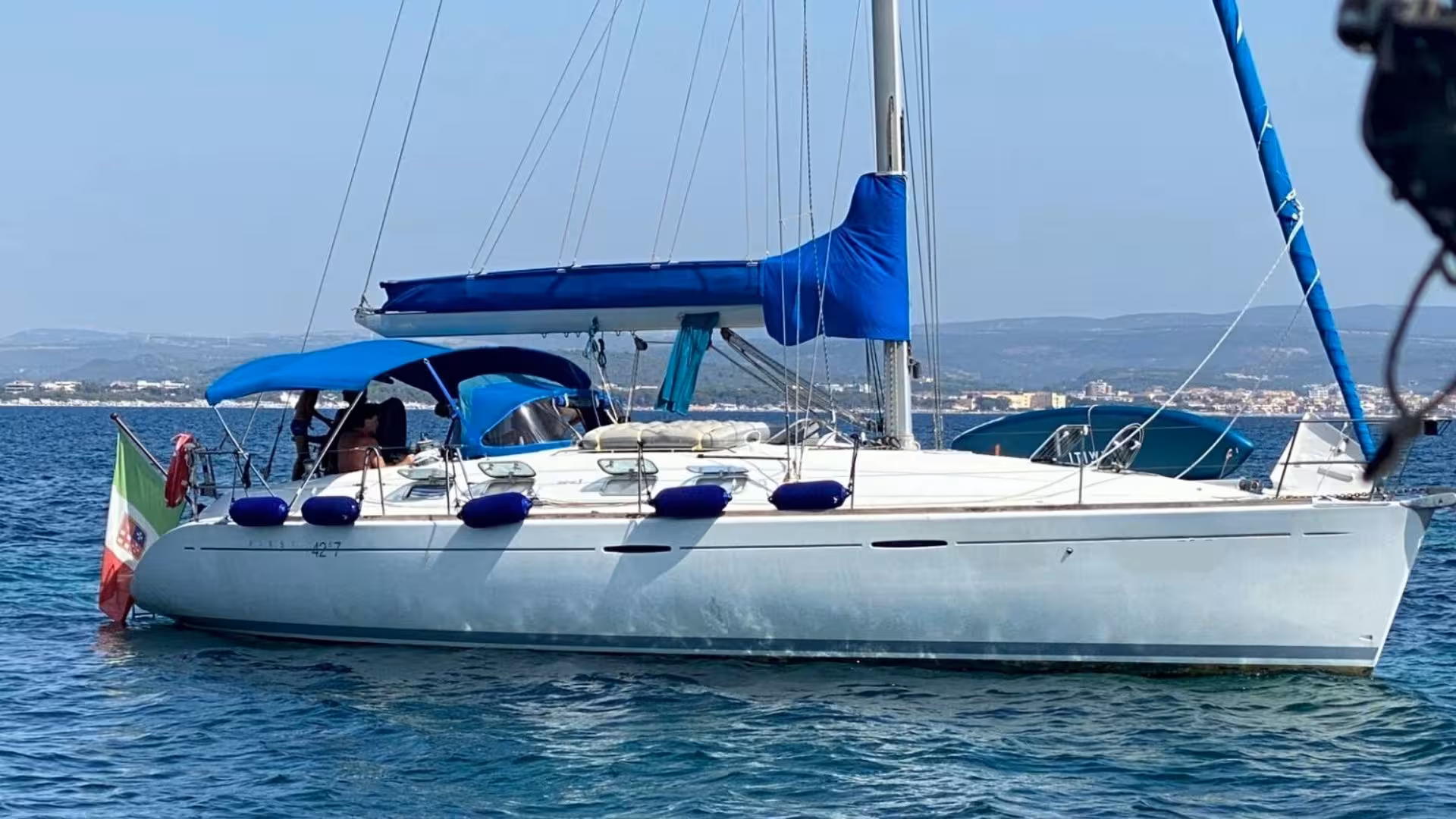 Elegant sailboat with blue accents moored in Alghero's scenic waters, promising a memorable excursion.