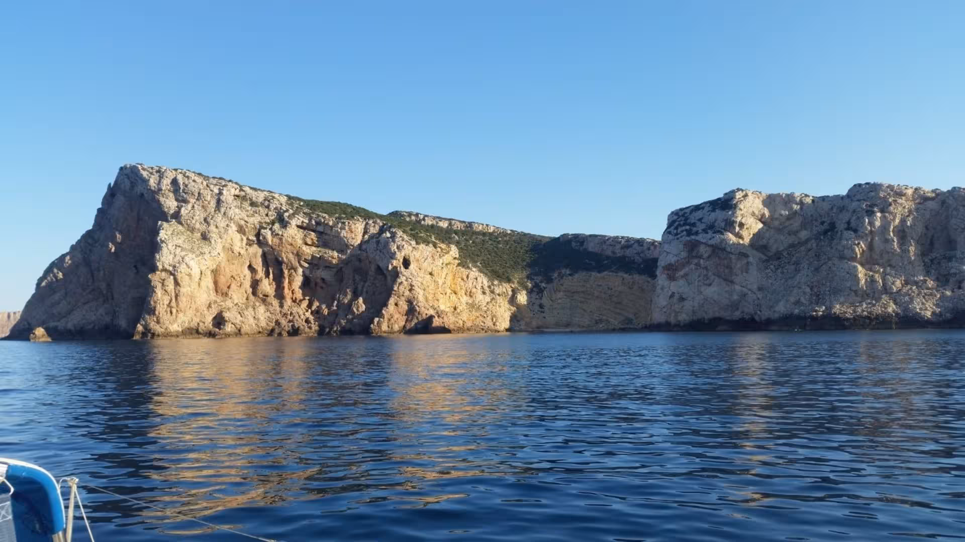 Admire stunning coastal cliffs under a clear blue sky on an Alghero sailboat excursion.