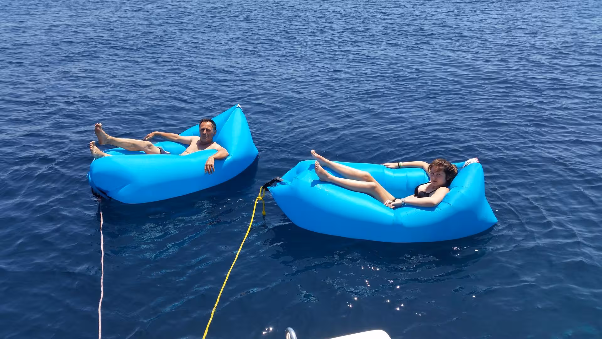 Relax on inflatable loungers in the crystal-clear waters during a sailboat excursion from Alghero.