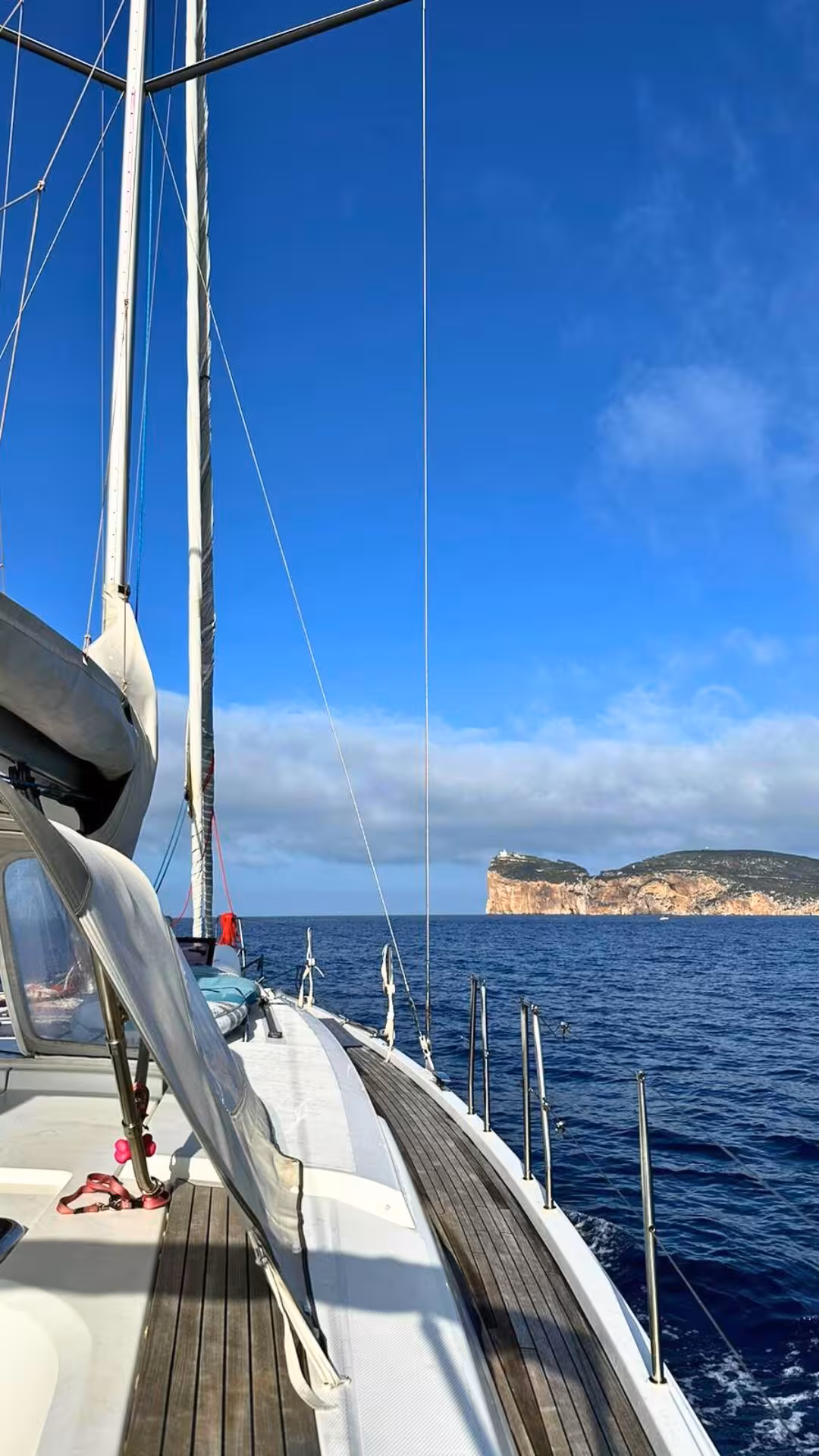 Sailing boat gliding over clear Mediterranean waters near Alghero with scenic cliffs under a sunny blue sky.