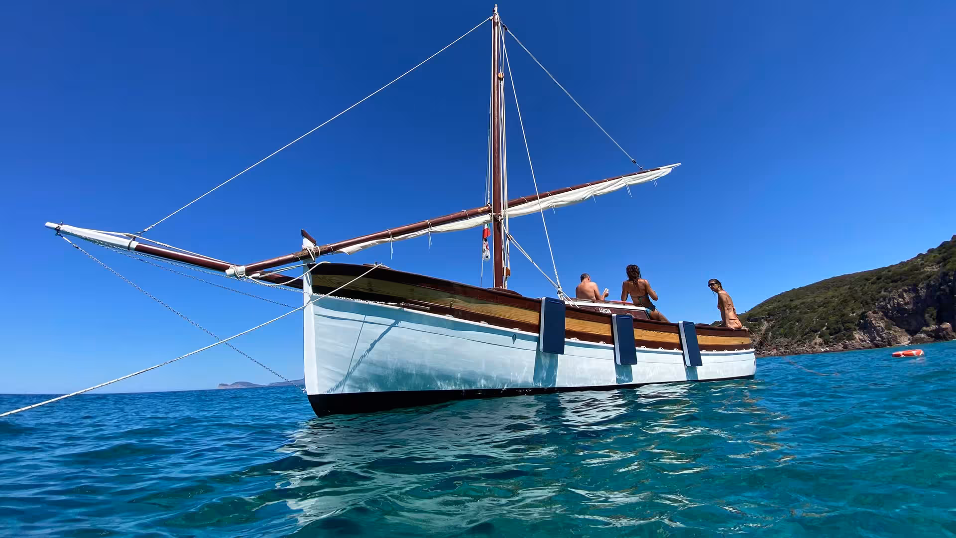 Tourists relaxing on a sailing boat off Sardinia's coast during a 4-hour Alghero tour in vibrant blue waters.