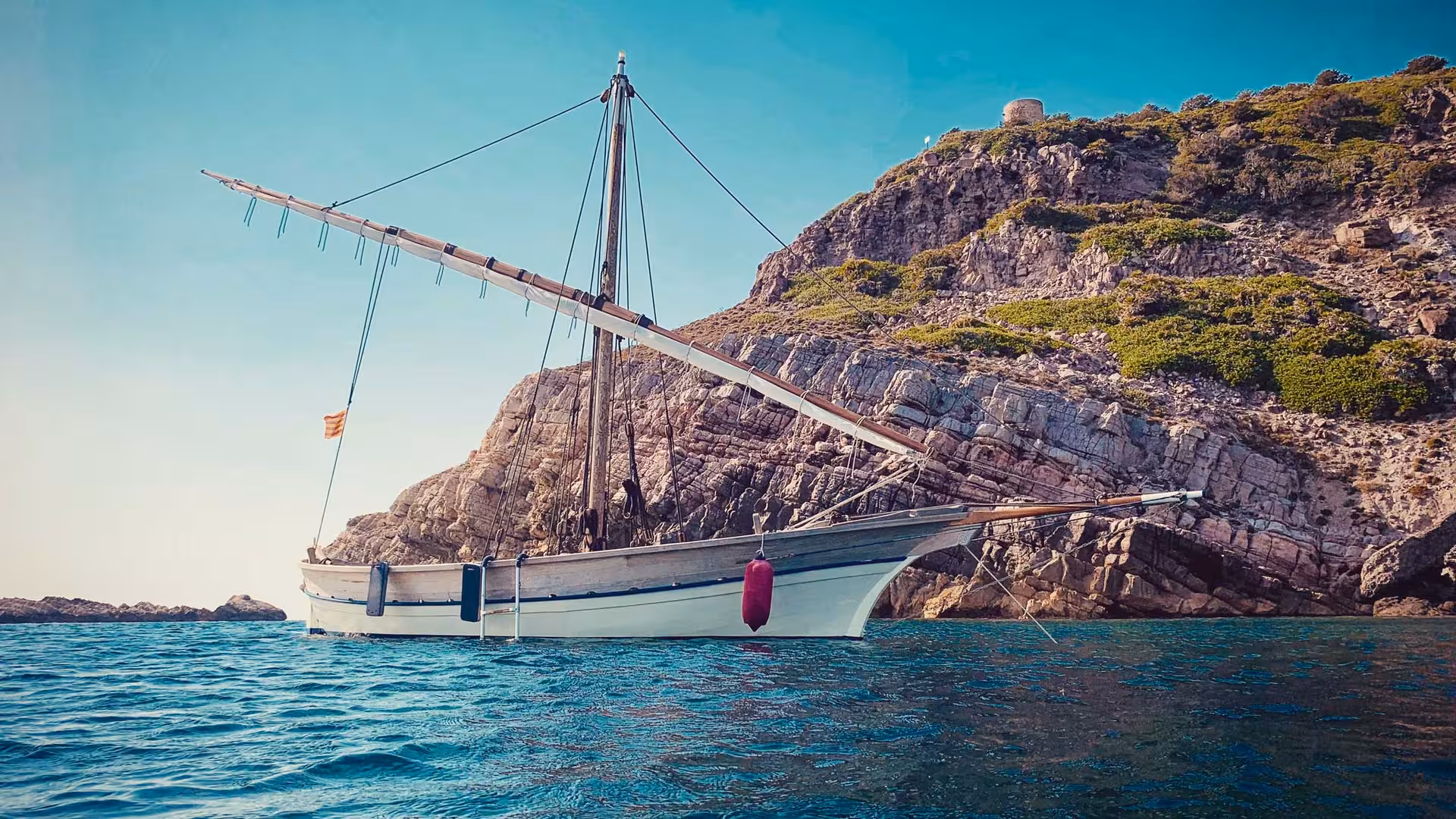 Traditional sailing boat near Alghero cliffs on a sunny 4-hour tour, ideal for exploring Sardinia's rugged coastline.