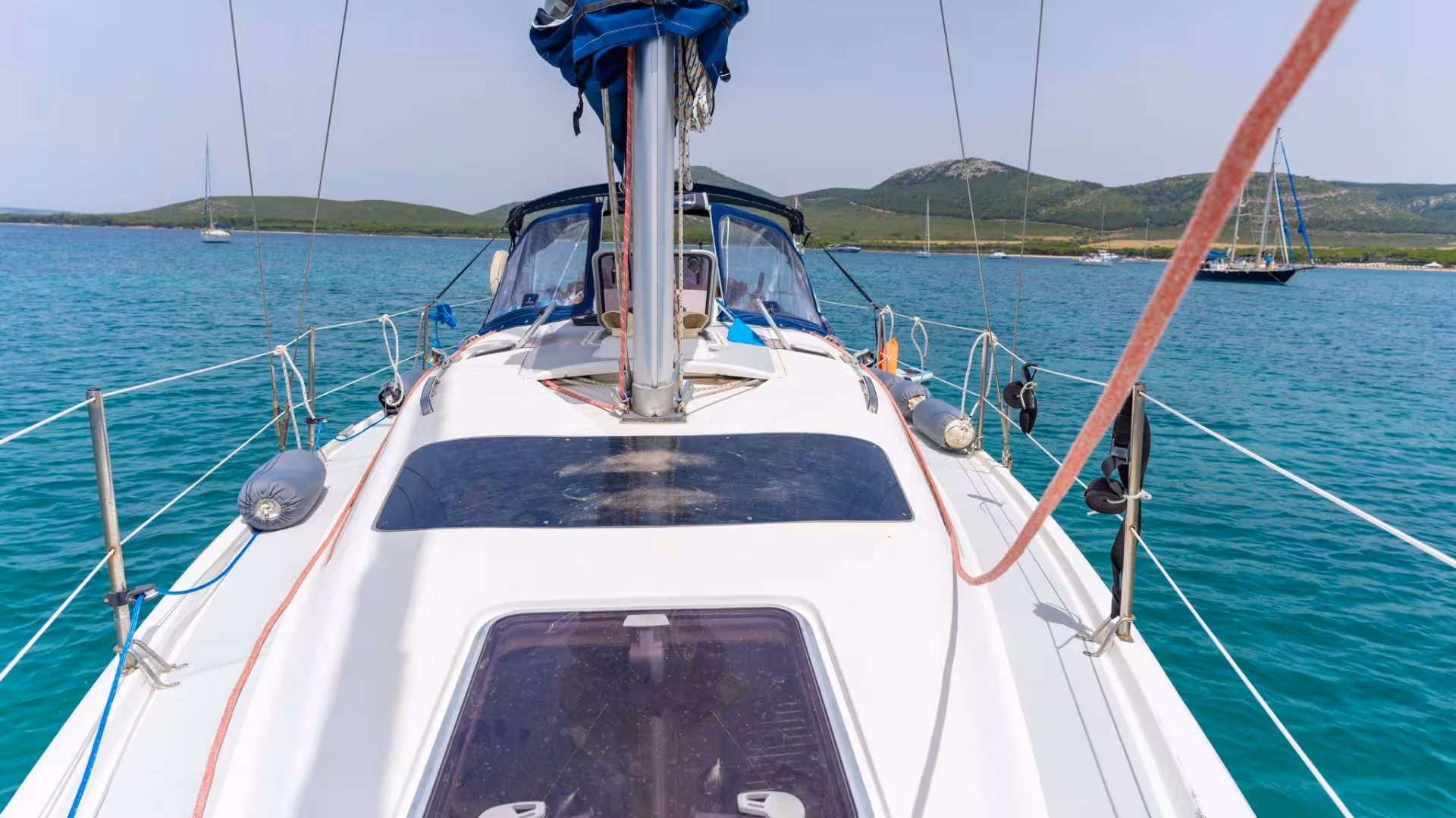 View from a yacht sailing in Porto Conte Park, Alghero, showcasing clear blue waters and distant sailboats.