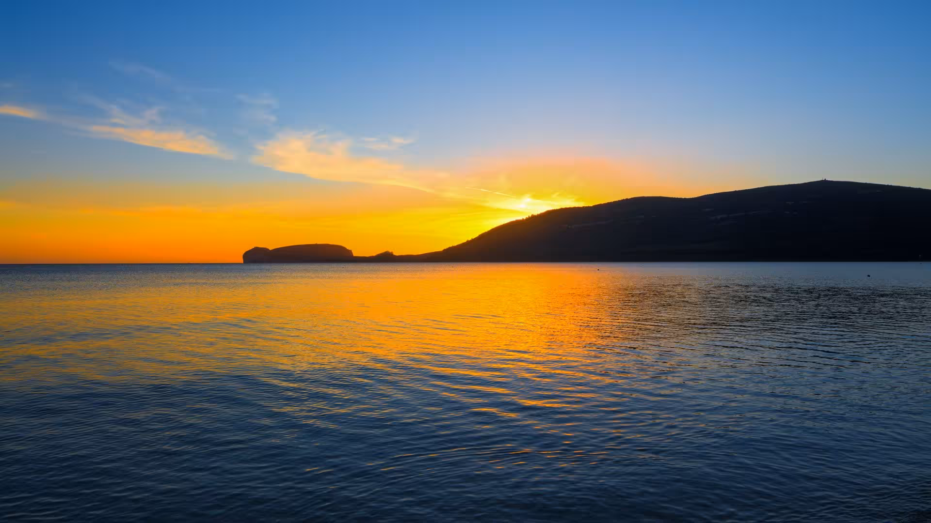 Breathtaking Alghero sunset over calm sea, ideal for private dinghy tours in Sardinia's picturesque coastline.