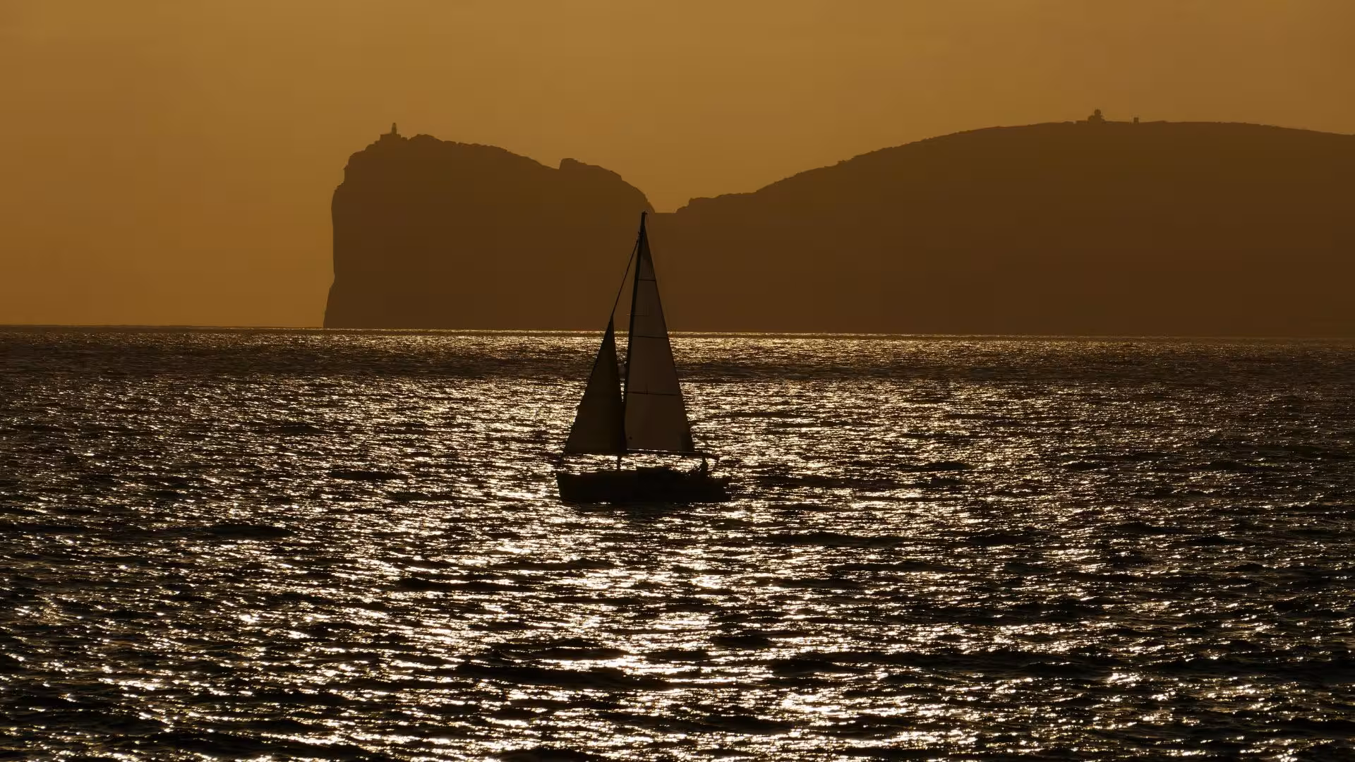 Silhouette of a sailboat during a golden sunset over the sea near Alghero, perfect for a romantic sailing experience.