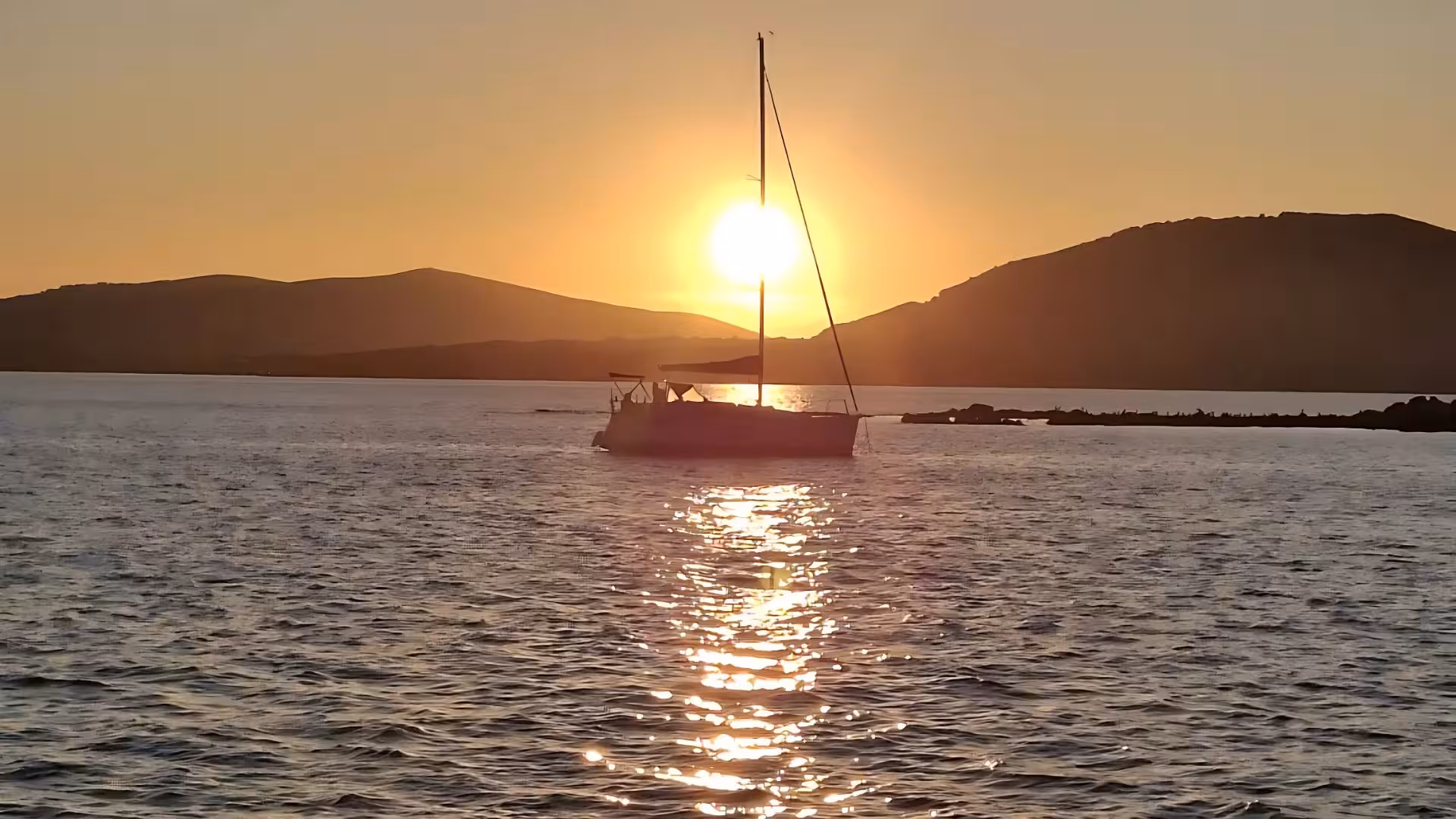 Silhouette of a sailboat at sunset on the tranquil waters near Alghero, perfect for a romantic evening sailing tour.