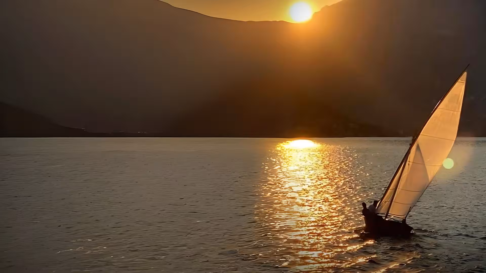 Silhouetted sailboat gliding on golden waters at sunset during an Alghero sailing tour with aperitif.