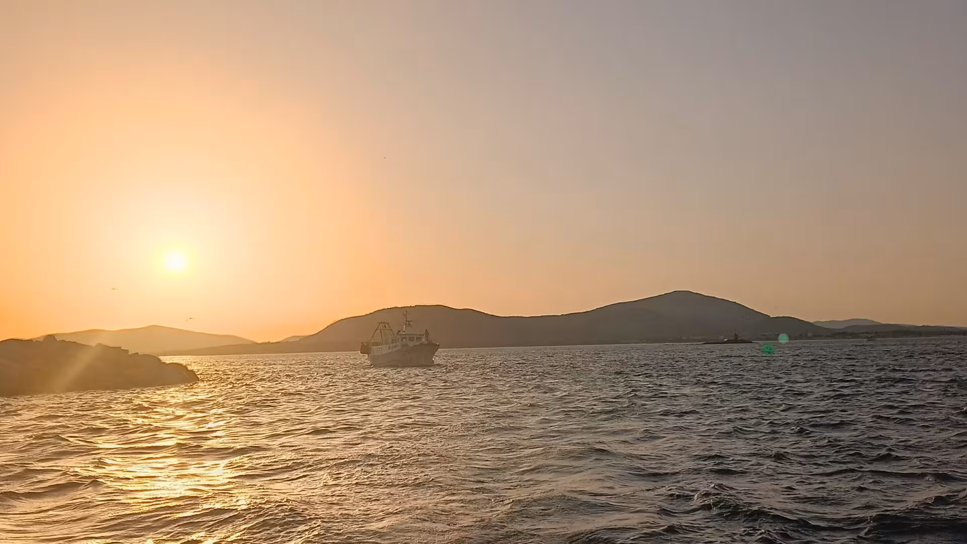 Boat sailing towards the horizon with a breathtaking sunset over Alghero's scenic coastline.