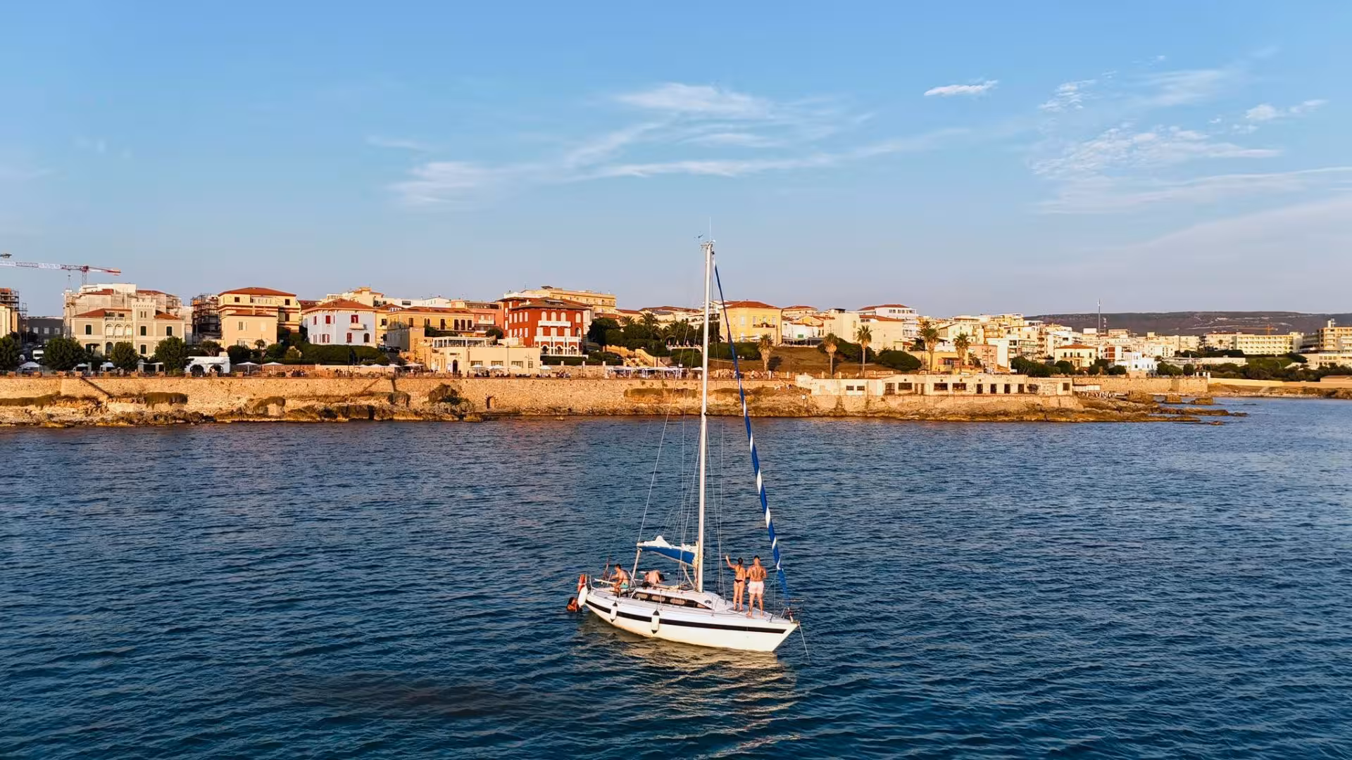 Sailboat cruising near Alghero's picturesque coastline during sunset, offering stunning views on a Fertilia sailing tour.