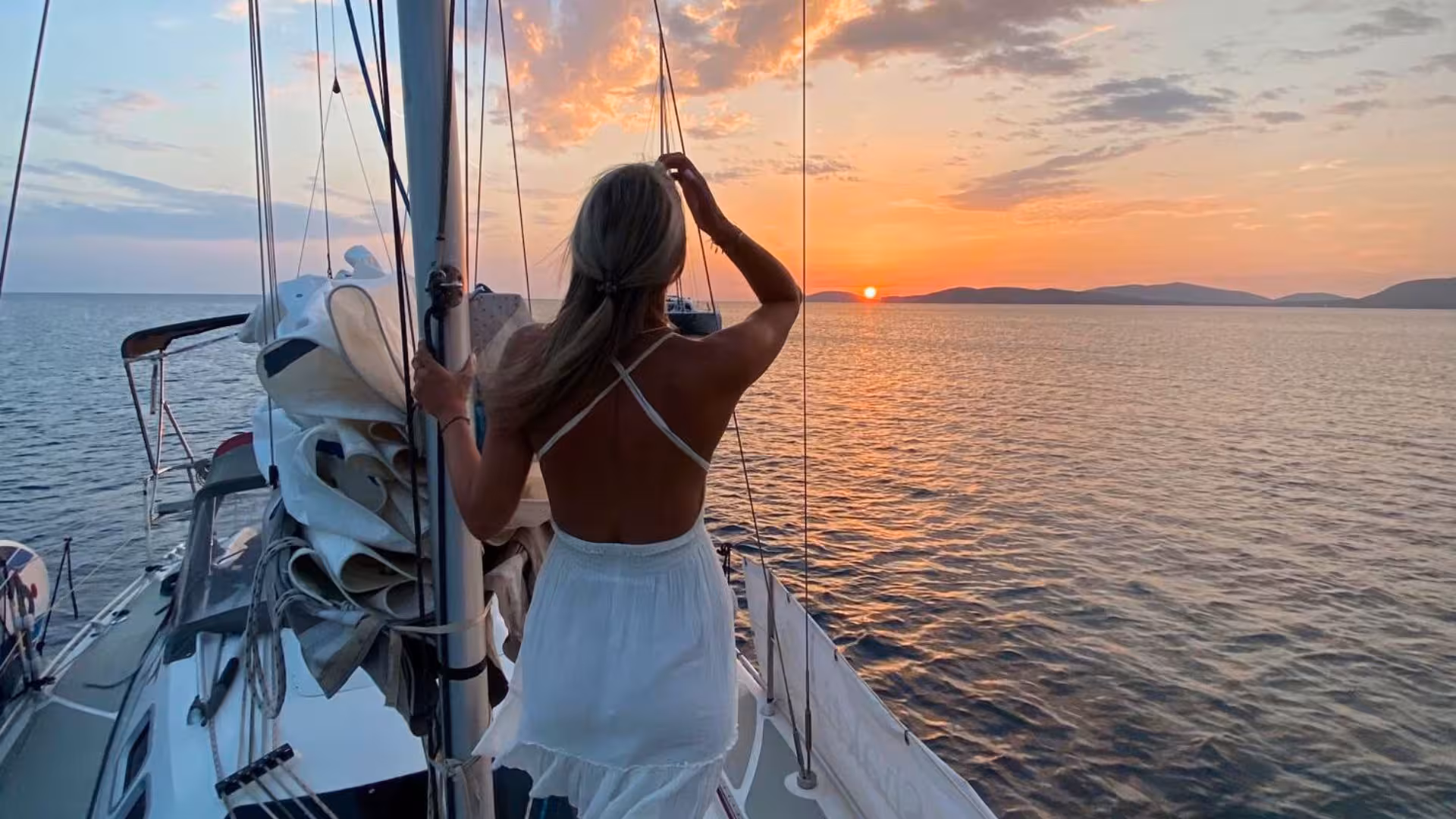Woman on a sailboat enjoying a vibrant sunset over the sea during Alghero sunset sailing tour.