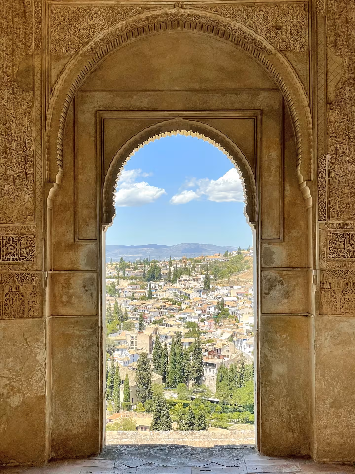 Stunning view from the Alhambra's arched window overlooking Granada, with picturesque cityscape and mountains.