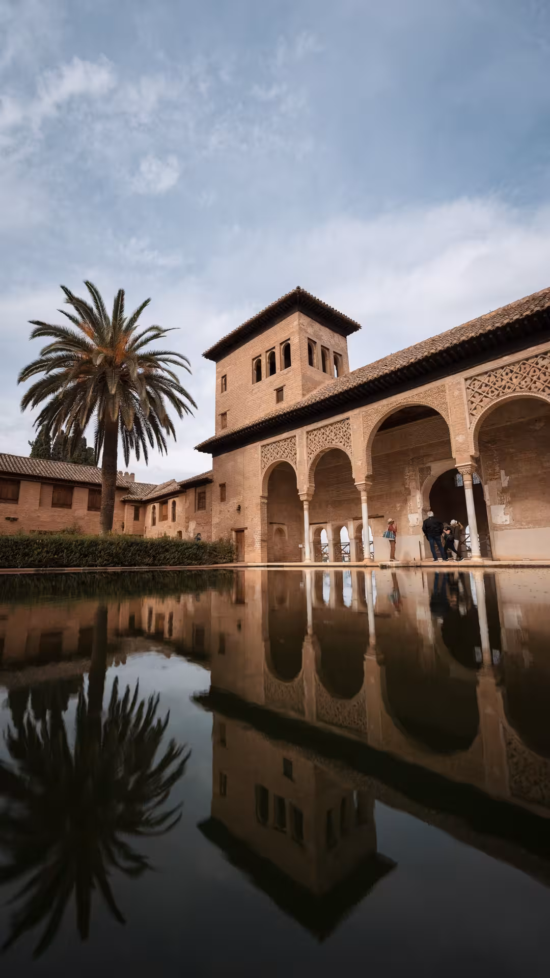 Reflected arches and palm tree in the serene pool of the Alhambra's Nasrid Palaces courtyard.