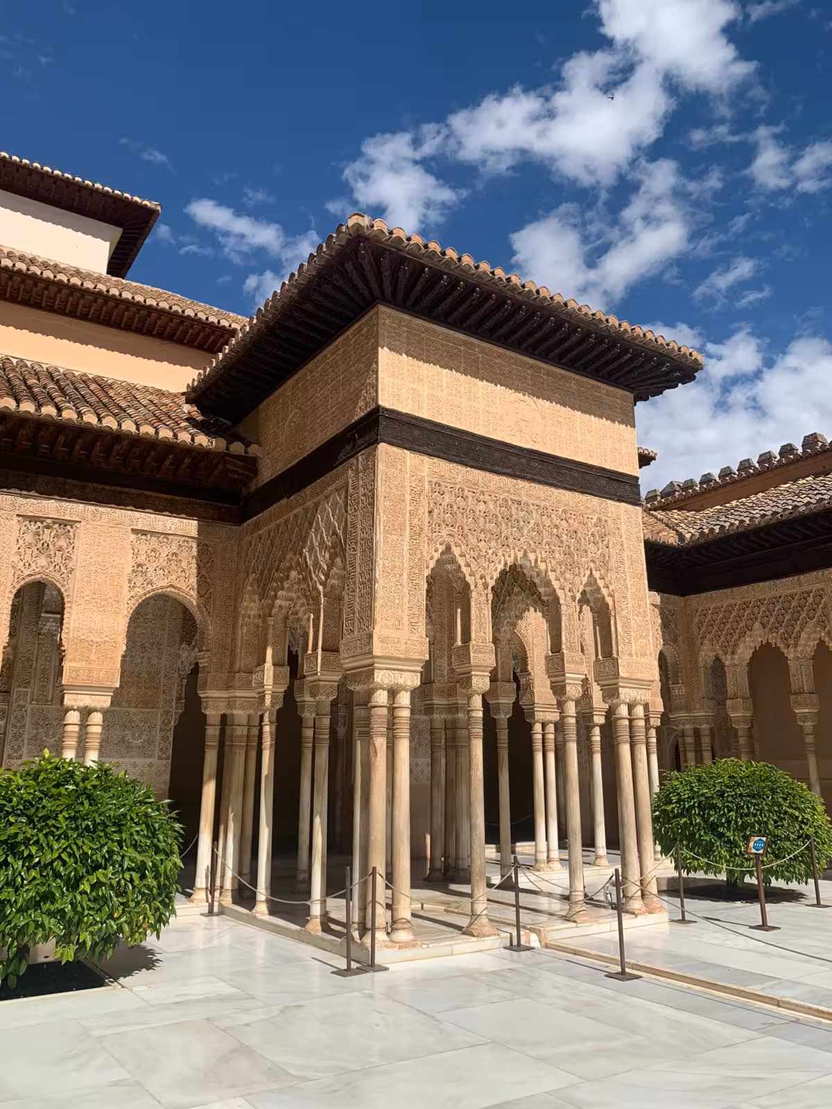 Intricate columns and detailed arches of Alhambra's Nasrid Palaces under a clear blue sky in Granada.