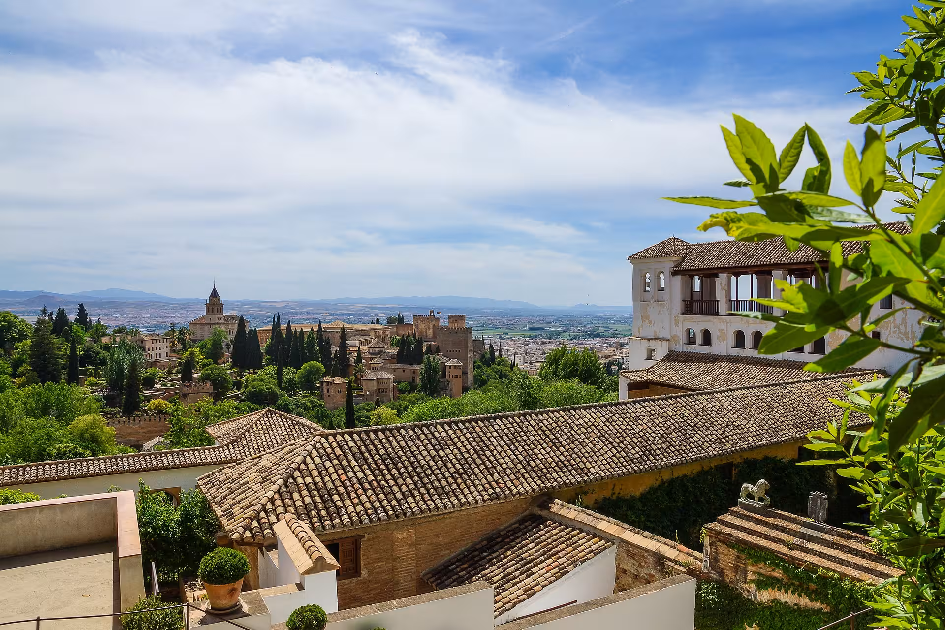 Panoramic view of Alhambra's stunning architecture amidst verdant gardens and distant mountains in Granada, Spain.