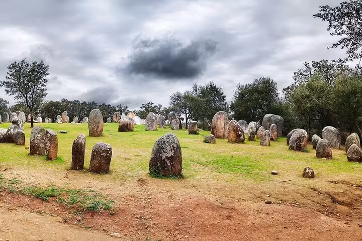 Scenic view of Almendres Cromlech prehistoric stone formations in Évora, under a dramatic sky, ideal for private tours.