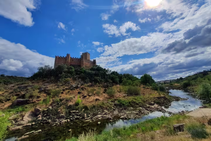 Scenic view of Almourol Castle on a hilltop surrounded by lush greenery and a river, part of the Tomar Knights Templar tour.