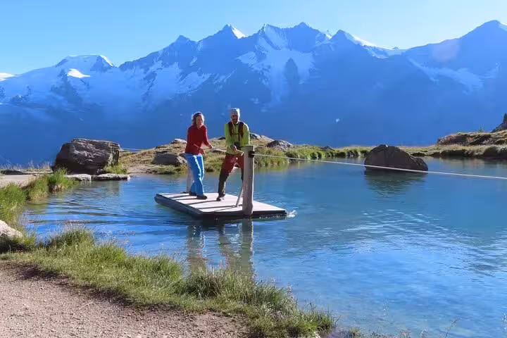 Travelers on a small raft on a clear alpine lake with snowy Swiss peaks, scenic stop on 4 day Alps trek