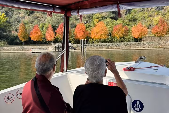 Couple photographing vibrant autumn foliage along the Douro River during a cultural guided boat tour of the Alto Douro Wine Region.