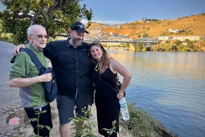 Happy tourists posing by the Douro River with historic bridge and golden vineyard hillsides on guided tour