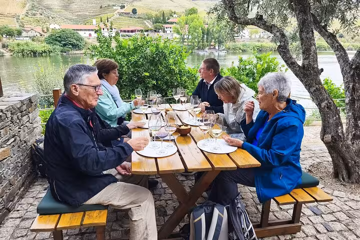 Guided tour group enjoying outdoor wine tasting by the scenic Douro River in Alto Douro wine region Portugal