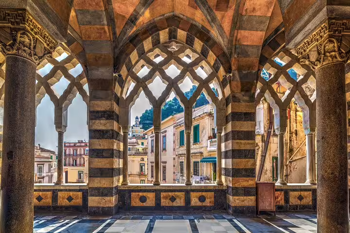 Moorish arches of Amalfi Cathedral cloister framing colorful historic houses on a sunny Amalfi Coast guided walking tour