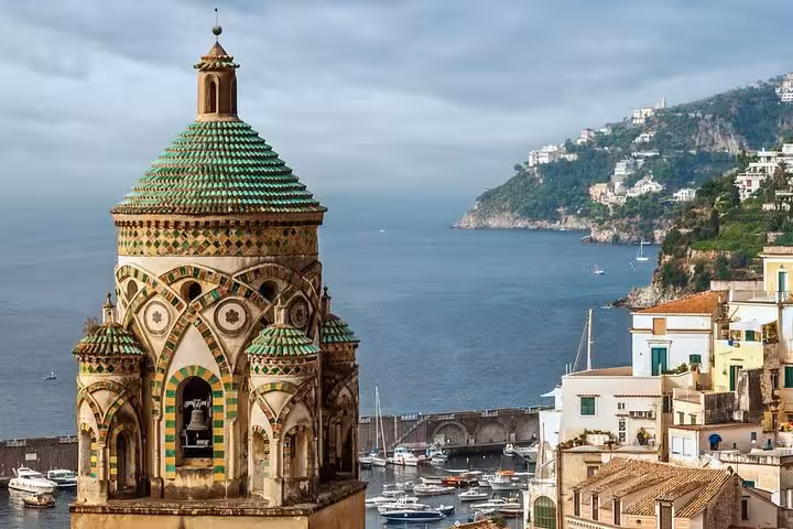 Scenic view of a historic bell tower overlooking the Amalfi Coast with boats and lush hills in the background.