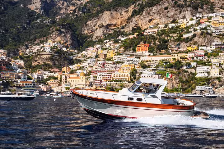 A boat cruising near the scenic cliffs and vibrant buildings of Positano on the Amalfi Coast during a sunny day tour.