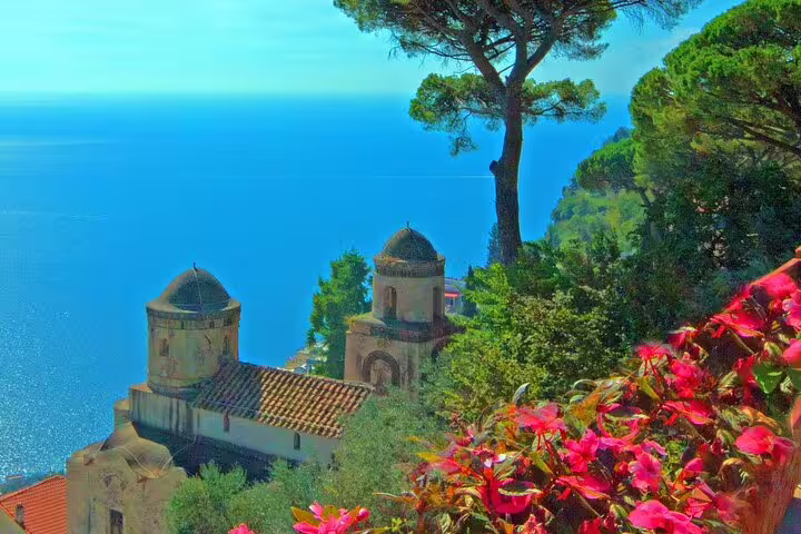 Panoramic view of Amalfi Coast church domes surrounded by lush greenery and pink flowers above the blue sea