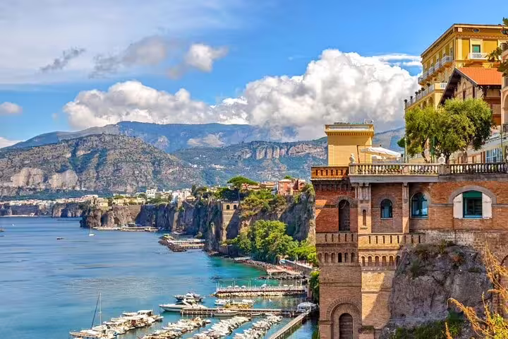 Cliffside buildings and marina along the Amalfi Coast with turquoise waters and mountains in background