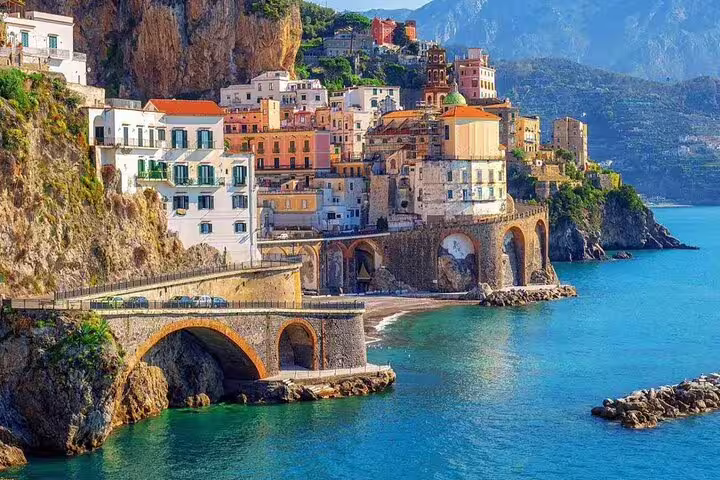 Colorful cliffside buildings of Atrani on the Amalfi Coast with stone arched bridge over turquoise sea