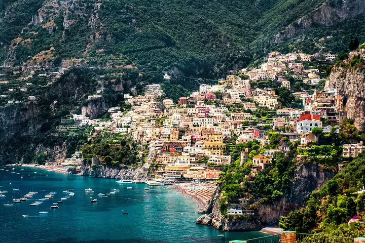Colorful cliffside buildings of Positano overlook the turquoise Amalfi Coast waters with boats below