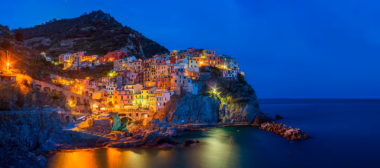 Twilight view of colorful cliffside village on the Amalfi Coast, Italy, with glowing lights reflecting on the calm Mediterranean Sea