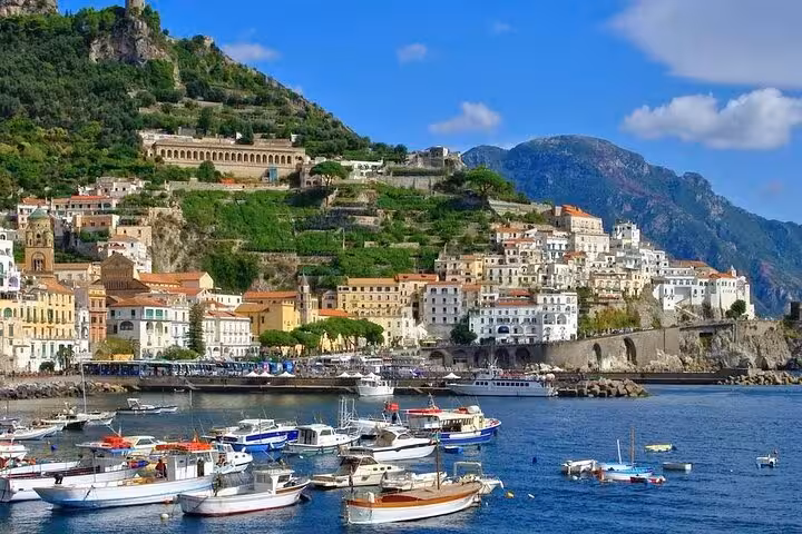 Vibrant coastal view of Amalfi with colorful boats and hillside architecture under a clear blue sky.