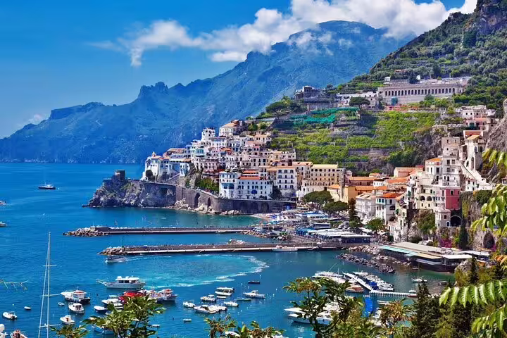 Colorful buildings cascading down cliffs to Amalfi Coast harbor with turquoise waters and moored boats