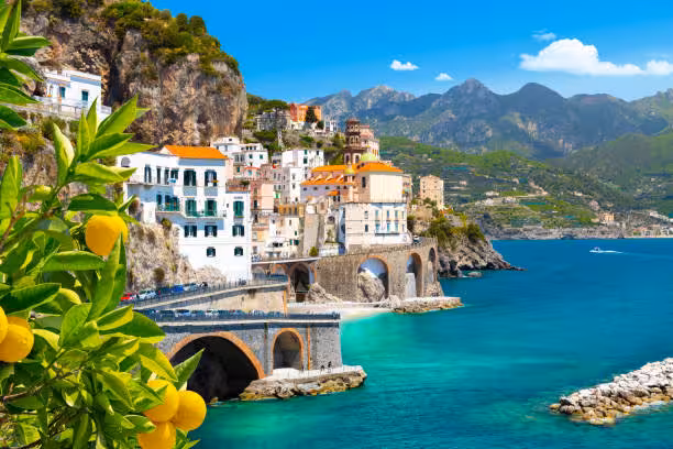 Scenic view of Amalfi Coast with vibrant lemons, colorful cliffside buildings, and turquoise sea under a clear blue sky.