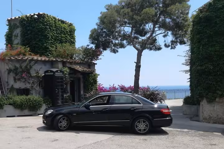 Luxury car parked by a picturesque villa with vibrant greenery and sea view on the Amalfi Coast tour.