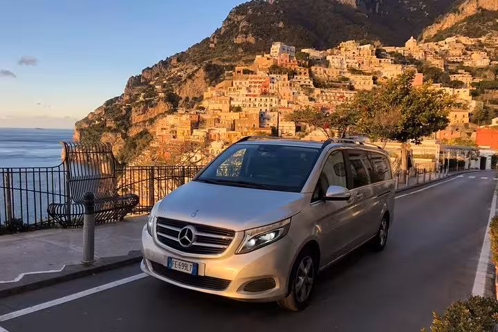 Luxurious minivan parked on a scenic road with Positano's colorful cliffside houses in the background on the Amalfi Coast.