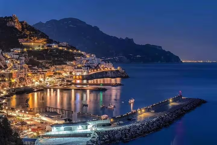 Amalfi Coast town glowing at night with golden lights reflecting on calm Mediterranean sea