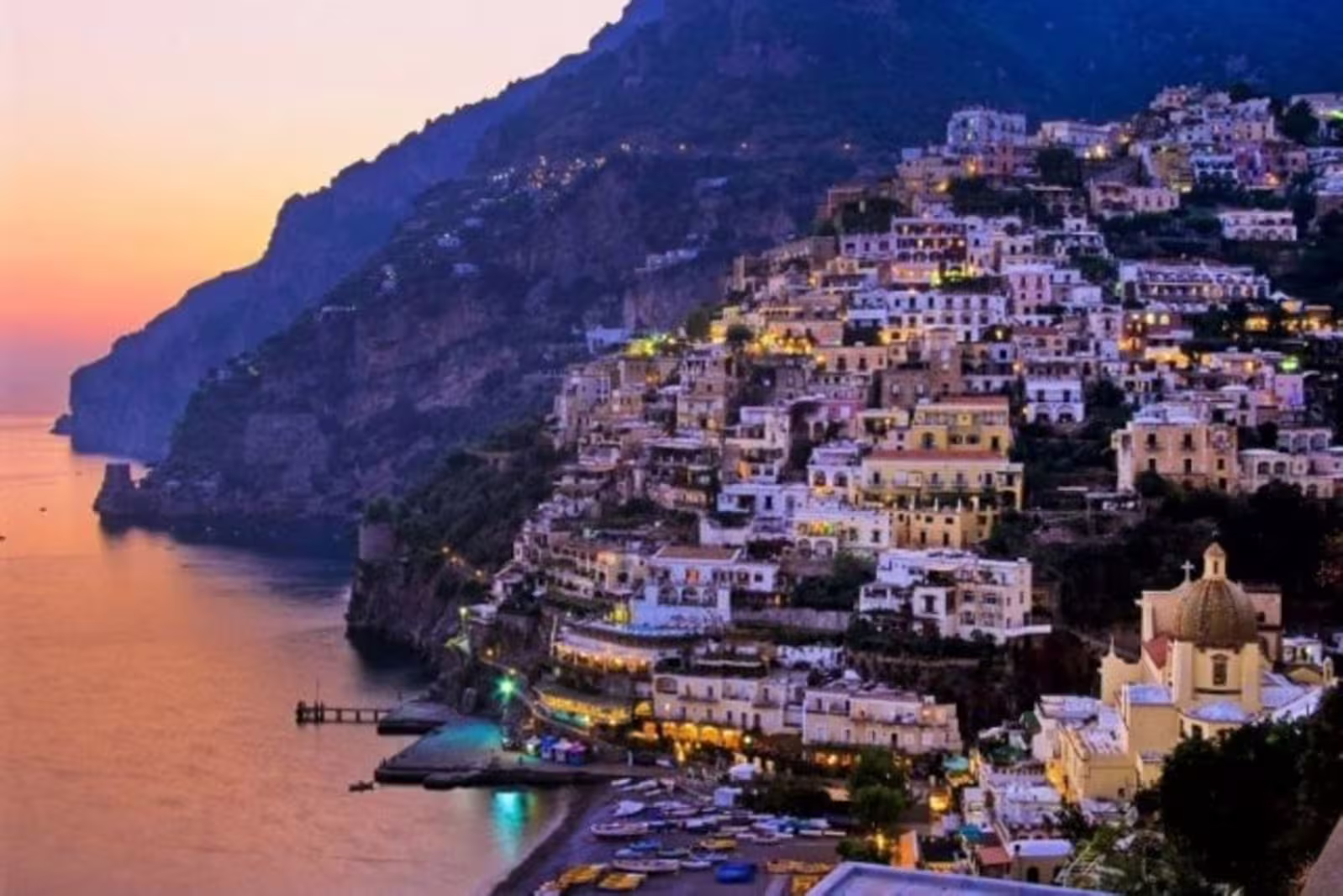 Romantic sunset over illuminated Positano village and calm sea on a shared Amalfi Coast private evening tour in Italy