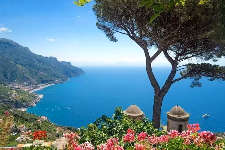 Breathtaking panorama of the Amalfi Coast from Ravello, featuring a picturesque tree and vibrant flowers against the azure sea.