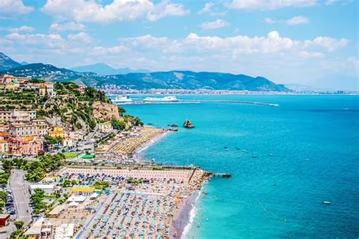 Aerial view of Amalfi Coast seaside village with colorful buildings, packed beach umbrellas, and turquoise Mediterranean Sea
