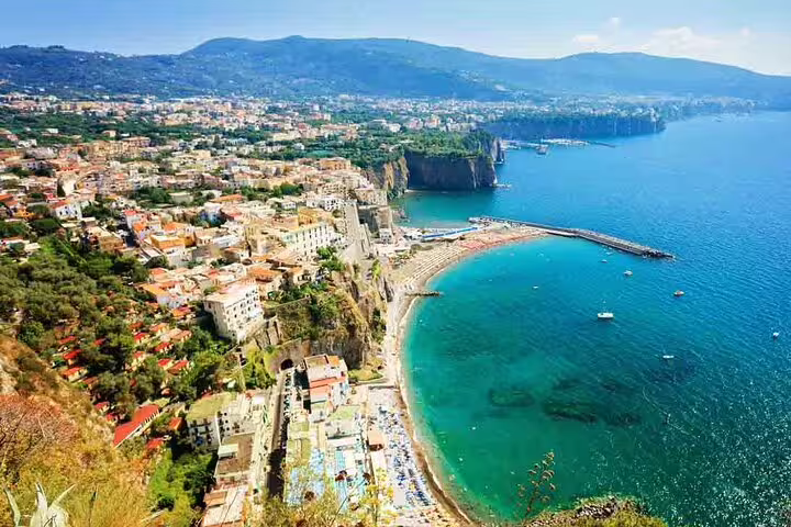Aerial view of Sorrento coastline with turquoise waters, cliffside buildings, and beach along the Amalfi Coast