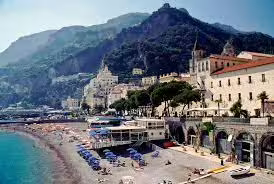 Scenic Amalfi Coast beach near Sorrento with sun loungers, historic cliffside houses and mountains seen from a boat tour