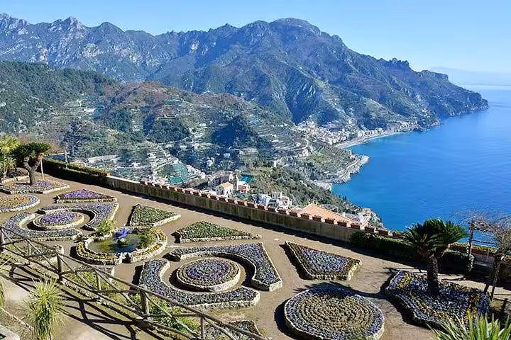 Scenic view of Amalfi Coast from a garden terrace, featuring the coastline and lush hills under a clear blue sky.