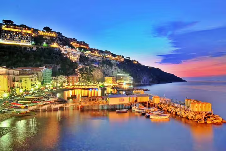 Sorrento coastal town illuminated at dusk with boats in harbor and cliffside hotels on Amalfi Coast