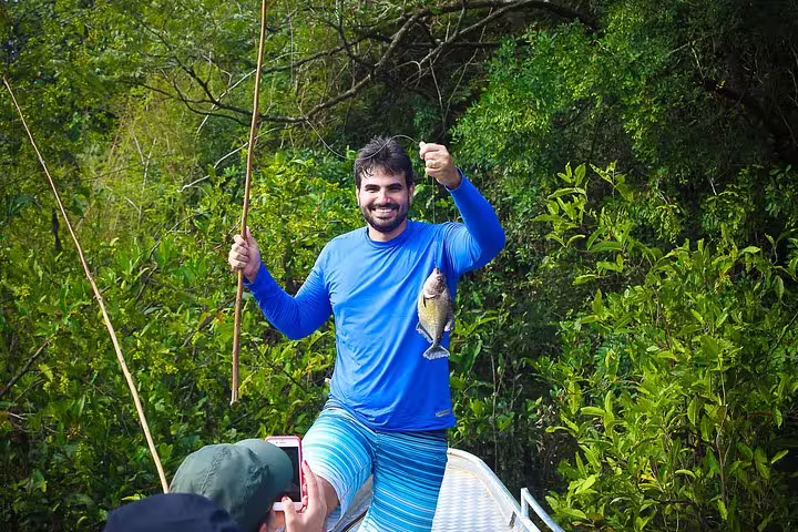 Happy angler holding a fish on a boat in the lush Amazon jungle, showcasing the adventure at Tapiri Rio Negro Lodge.