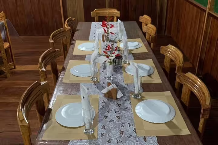 Rustic dining setup at Amazon Mamori Lodge with wooden table, elegant tableware, and vibrant floral centerpiece.