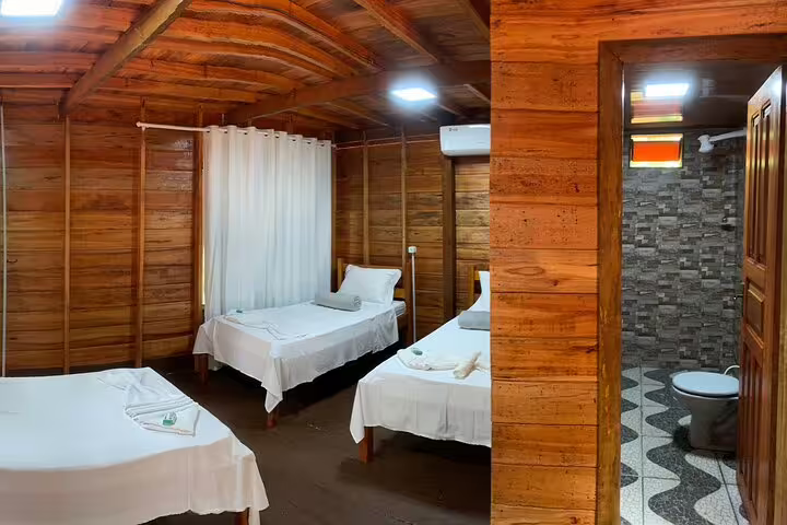Cozy wooden cabin interior at Amazon Mamori Lodge features comfortable beds and en-suite bathroom for a relaxing stay.