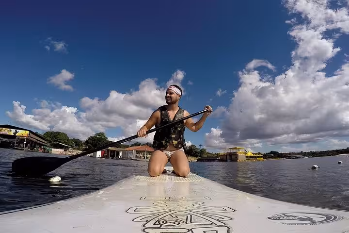 Stand up paddling on the Amazon River, traveler kneeling on SUP board with paddle and dramatic clouds